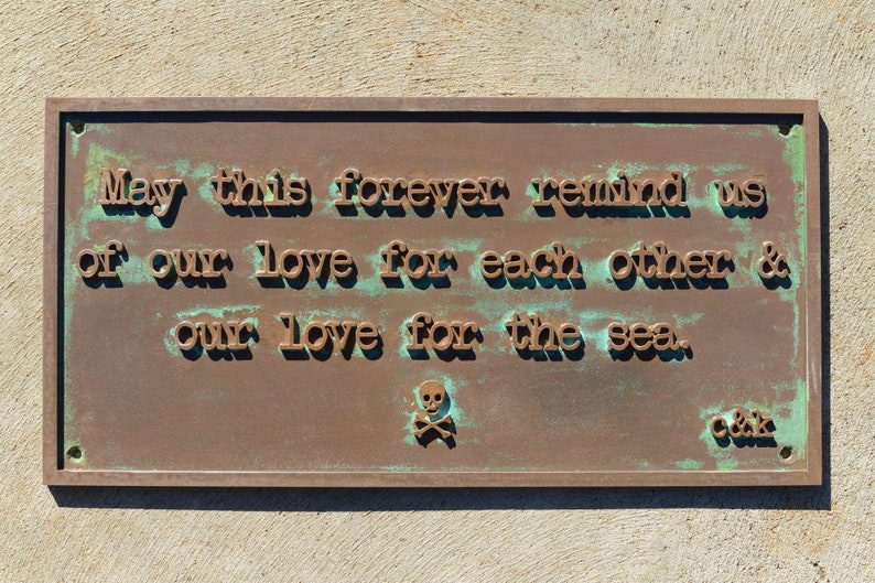 May include: A rectangular bronze plaque with embossed text that reads "May this forever remind us of our love for each other & our love for the sea." A skull and crossbones symbol is below the text.
