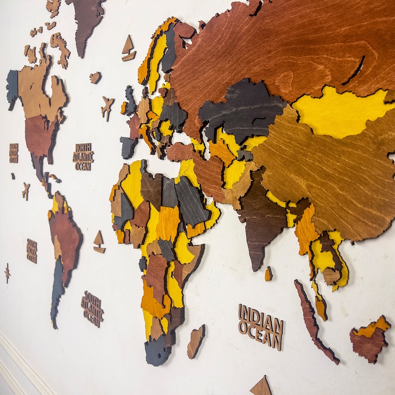 Detail shot of colorful 3D wooden world map wall art — Europe, Africa and Asia in vibrant layered birch plywood with Indian Ocean label, angled perspective showing dimensional depth