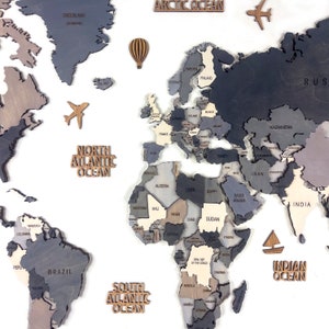 A wooden world map with countries in shades of gray, brown, and beige. The map includes wooden cutouts of an airplane, hot air balloon, and sailboat. The oceans are labeled with wooden text cutouts.
