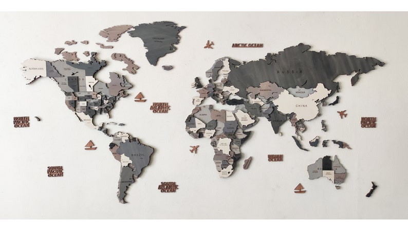 May include: A wooden world map wall decor in shades of gray, brown, and white. The map features individual country cutouts and includes decorative elements like airplanes and boats. The map is mounted on a white wall.