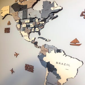 Close-up of dark grey 3D wooden world map showing North and South America with USA states and Brazil in layered grey tones