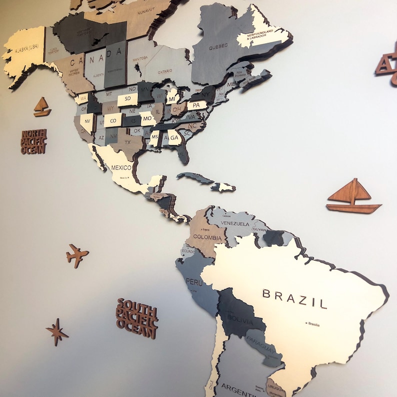 Close-up of dark grey 3D wooden world map showing North and South America with USA states and Brazil in layered grey tones