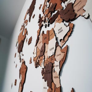 Close-up of 3D wooden world map showing Africa with engraved country names in mixed brown tones on a white wal