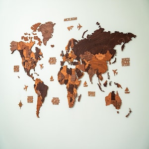Large 3D wooden world map wall decor in mixed brown tones — laser-cut birch plywood with country names, ocean labels, and decorative wooden planes and sailboats