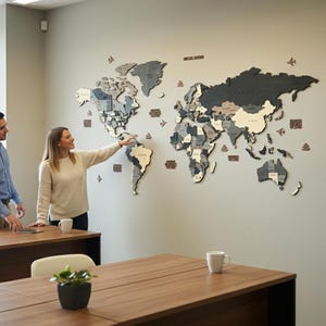 3D wooden world map in dark grey tones displayed in a modern office, woman pointing at the map