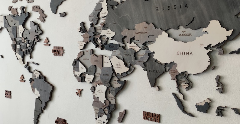 May include: A wooden world map with countries in shades of gray, brown, and beige. The map includes the names of countries and oceans. The word "CHINA" is visible on the map.
