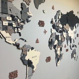 Dark grey 3D wooden world map wall art — full view with USA states, Brazil, ocean labels and decorative planes and sailboats in layered grey birch plywood