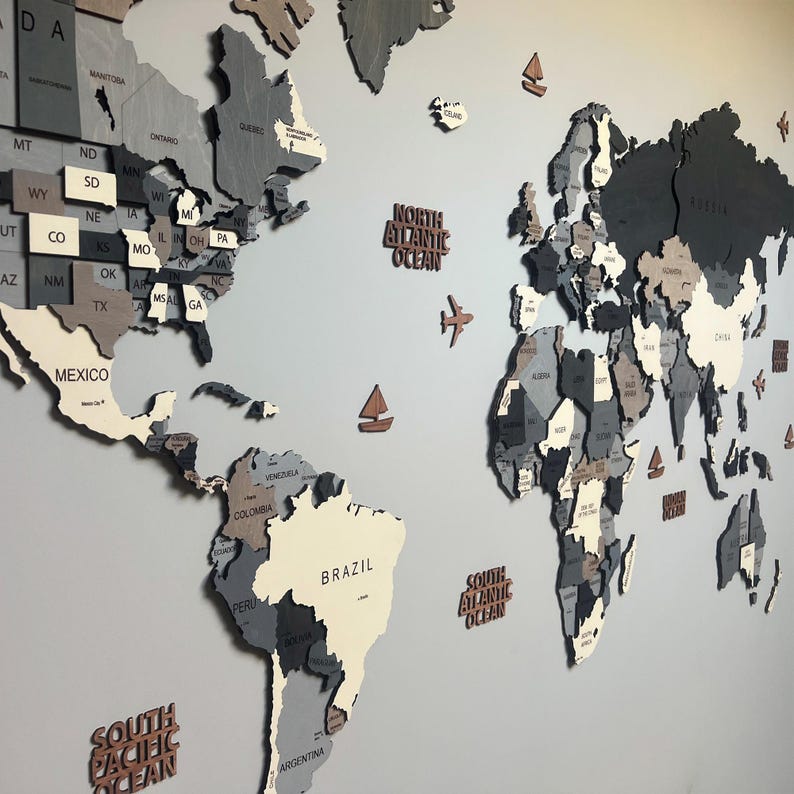 Dark grey 3D wooden world map wall art — full view with USA states, Brazil, ocean labels and decorative planes and sailboats in layered grey birch plywood