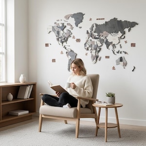 Woman reading in an armchair beneath a large 3D wooden world map in dark grey tones in a minimalist Scandinavian living room