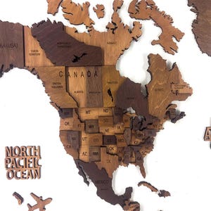 Close-up of 3D wooden world map showing USA and Canada with state and province divisions in warm brown tones