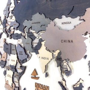 Detail shot of dark grey 3D wooden world map — laser-engraved China, India, Mongolia and Middle East countries in layered grey and white birch plywood