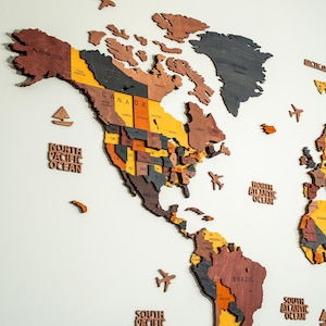 Detail shot of colorful 3D wooden world map — USA states and Canadian provinces laser-engraved in vibrant yellow, orange, brown and grey layered birch plywood