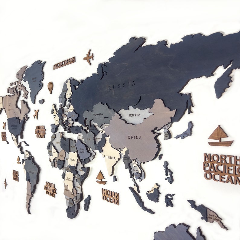 May include: A wooden world map with countries in shades of gray, blue, and beige. The map includes labeled oceans and continents, with small wooden airplane, hot air balloon, and sailboat accents. The map is mounted on a white background.