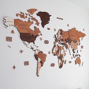 3D wooden world map wall decor in warm brown tones — layered birch plywood with white spacing between countries, decorative planes and compass
