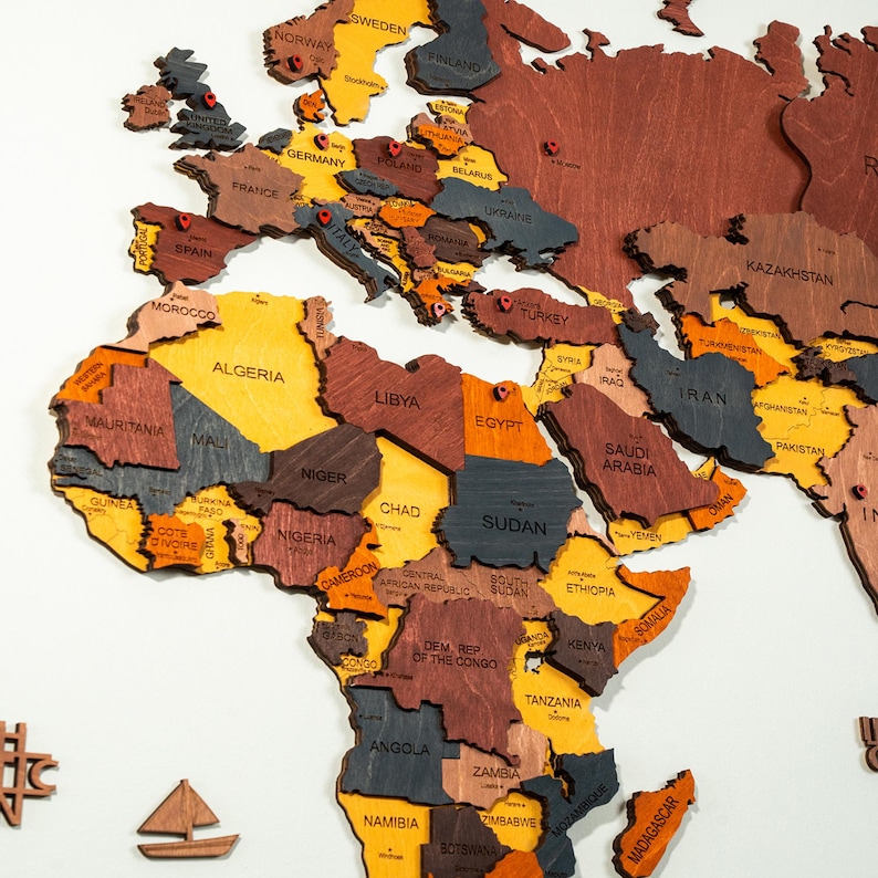 Detail shot of colorful 3D wooden world map — laser-engraved country names across Europe, Africa and Middle East in vibrant yellow, orange, brown and grey wood tones with red location pins