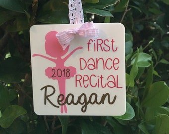 Peut inclure: Ornement carré blanc avec une silhouette de ballerine rose, le texte "first dance recital 2018 Reagan" et un nœud rose.