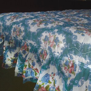 Puede incluir: Un cubrecama blanco con un patrón azul y floral. El cubrecama tiene un borde con volantes y está hecho de una tela transparente.