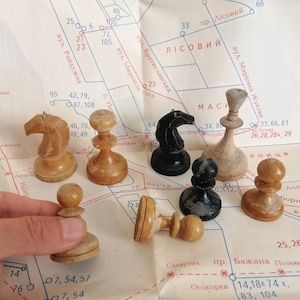 Puede incluir: Una colección de piezas de ajedrez de madera sobre un mapa. Las piezas incluyen un caballo, un alfil, un peón y un rey. El mapa está en ucraniano y presenta nombres de calles y números.