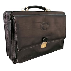 May include: A black leather briefcase with a gold lock and a gold embossed logo. The briefcase has a flap closure and a handle.