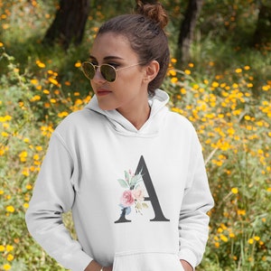 May include: White hooded sweatshirt with a black letter "A" decorated with pink, blue and green floral accents.