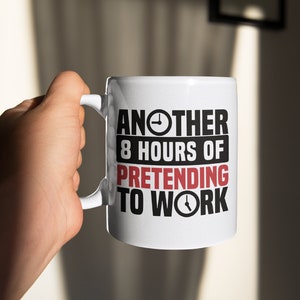 Op de afbeelding: Witte keramische mok met zwarte tekst die "Another 8 hours of pretending to work" luidt met een klokpictogram aan weerszijden van de tekst.