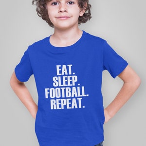 May include: A royal blue t-shirt with white text that reads "EAT. SLEEP. FOOTBALL. REPEAT."