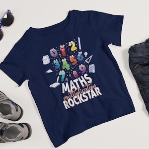 Può includere: T-shirt blu navy con una grafica colorata di numeri dei cartoni animati e articoli scolastici. Il testo recita "MATHS multiplication ROCKSTAR". Il design include uno zaino, una calcolatrice e un libro aperto.