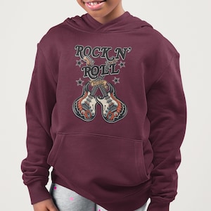 Op de afbeelding: Bordeaux hoodie met een afbeelding met de tekst "ROCK N' ROLL" boven twee gekruiste gitaren. De gitaren zijn rood, wit en zwart met het woord "MUSIC" ertussen. Sterren omringen de tekst en de gitaren.