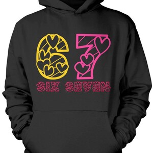 May include: Black hooded sweatshirt with the number "67" in yellow and pink. The "6" is filled with yellow hearts, and the "7" has pink hearts. The words "SIX SEVEN" are printed in pink below the numbers.