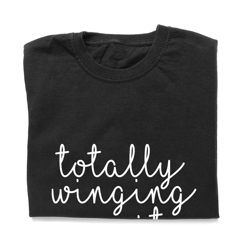 Puede incluir: Camiseta negra con el texto "totally winging it" en blanco.