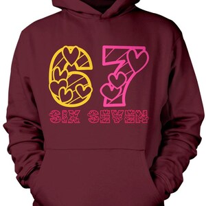May include: Burgundy hoodie with a front graphic. The graphic features the number 67 in yellow and pink, with heart shapes inside the numbers. The words "SIX SEVEN" are below the numbers in pink.