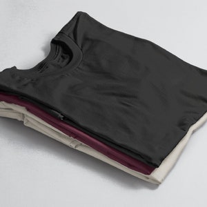 Puede incluir: Una pila de tres camisetas dobladas en negro, burdeos y beige.