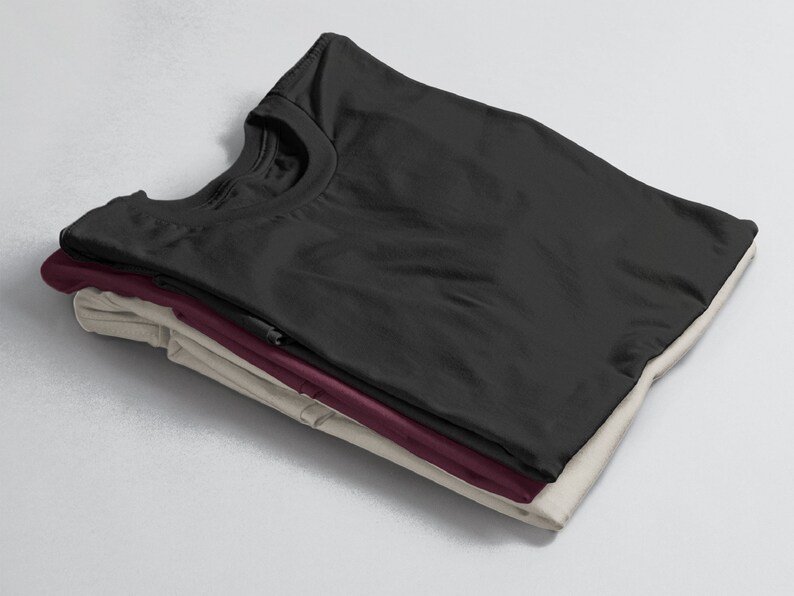 Puede incluir: Una pila de tres camisetas dobladas en negro, burdeos y beige.