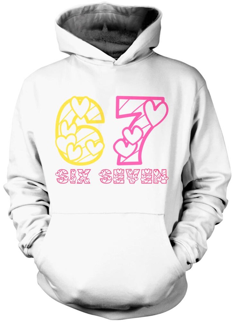 May include: White hoodie with a drawstring hood and a kangaroo pocket. The front features the number "67" in yellow and pink, with heart-shaped cutouts. The text "SIX SEVEN" is printed below in pink.