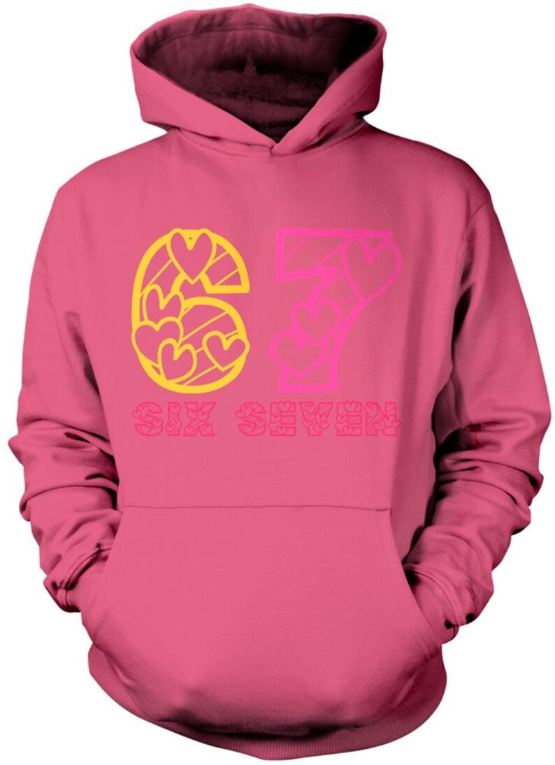 May include: Pink hooded sweatshirt with the number 67 in yellow and pink, with heart-shaped designs. The words "SIX SEVEN" are printed below the numbers. The sweatshirt has a front pocket and a hood.