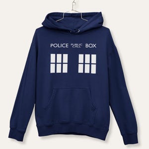 Op de afbeelding: Marineblauwe hoodie met een witte afbeelding van een politie-telefooncel. De tekst "POLICE PUBLIC CALL BOX" staat boven de afbeelding. De hoodie heeft een voorzak en een capuchon met trekkoord.