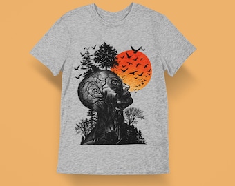 May include: A heather grey t-shirt featuring a black ink illustration of a human head and neck with tree-like veins, surrounded by a forest silhouette and a flock of birds flying towards a large, vibrant orange and red circular sun.