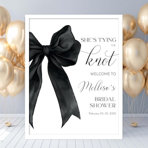 May include: A white sign with black text and a black bow. The text reads "She's tying the knot. Welcome to Melissa's Bridal Shower. February 05, 05 2025".