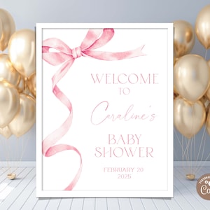 May include: A white sign with a pink ribbon bow and the text "Welcome to Caroline's Baby Shower February 20 2025".