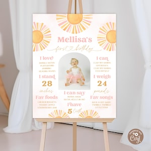 Könnte beinhalten: Personalisiertes Schild zum ersten Geburtstag mit Foto eines Babymädchens, Sonnenillustrationen und Details wie Größe (71 cm), Gewicht (10,9 kg) und Lieblingsspeisen. Auf einer Holzstaffelei.
