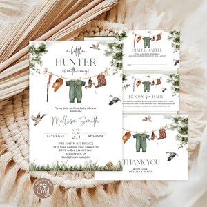 May include: A set of baby shower stationery featuring a hunting theme with watercolour illustrations of a rifle, hat, green onesie, and cowboy boots hanging on a clothesline, surrounded by ducks and greenery, with printed event details and text.