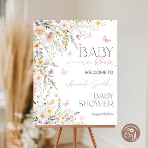 May include: A floral baby shower welcome sign with the text "Baby in Bloom" and "Welcome to Amanda Smith's Baby Shower" with the date "August 20, 20xx". The sign is decorated with watercolour flowers and butterflies.