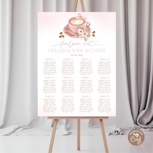 May include: A baby shower seating chart on an easel. The sign has a pink ombre background with a coffee cup illustration. The text reads "find your seat" and "Mellisa's Baby Shower 07.04 20xx". The chart lists table numbers and names.