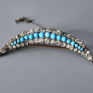 May include: A crescent-shaped brooch with a row of turquoise blue stones surrounded by clear rhinestones.