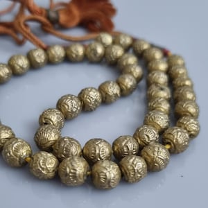 May include: A gold beaded necklace with a tassel. The beads are round and have a textured surface. The necklace is strung on a thin cord.