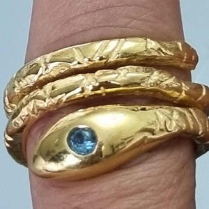 Op de afbeelding: Gouden slangenring met een blauwe edelsteen. De ring is gemaakt van drie banden, elk met een andere textuur.