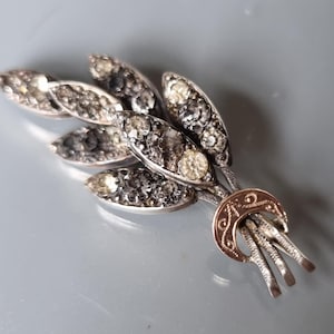 May include: A silver and gold pendant with a cluster of five leaves, each set with small clear rhinestones. The pendant has a crescent moon design at the bottom.