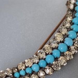 May include: A silver and turquoise brooch with a crescent shape. The brooch is made of small, faceted stones and features a row of turquoise stones.