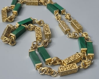 Könnte beinhalten: Eine goldfarbene Halskette mit rechteckigen grünen Steinakzenten und dekorativen goldenen Gliedern. Die Halskette hat ein sich wiederholendes Muster aus grünen Steinen und verzierten goldenen rechteckigen Gliedern, wodurch ein luxuriöses und elegantes Design entsteht.