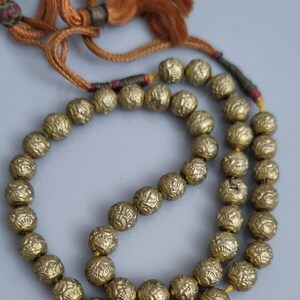 May include: A gold beaded necklace with a tassel. The beads are round and have a textured surface. The tassel is made of brown cord.